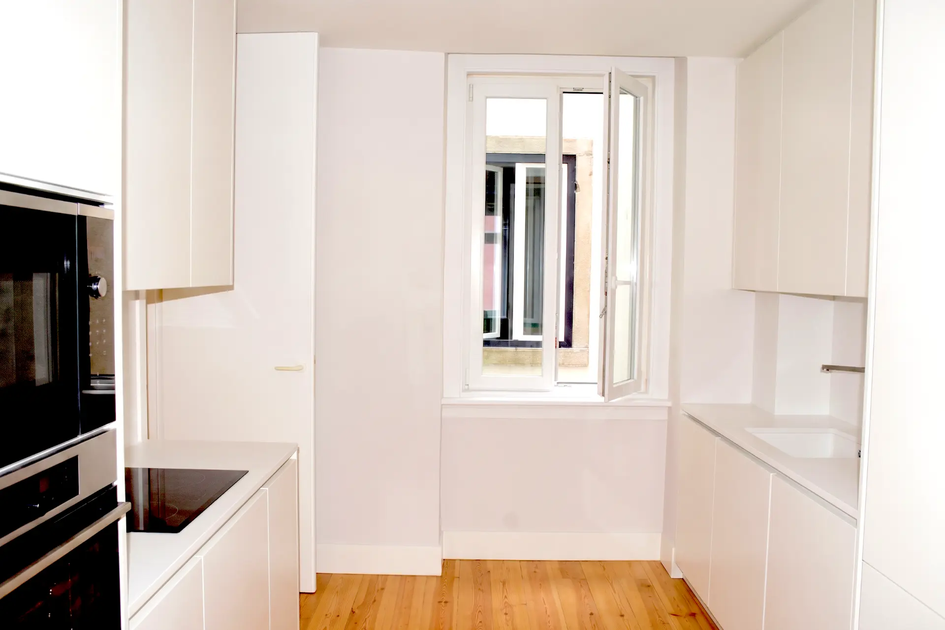 Cozinha com placa de indução, forno e janela para o saguão