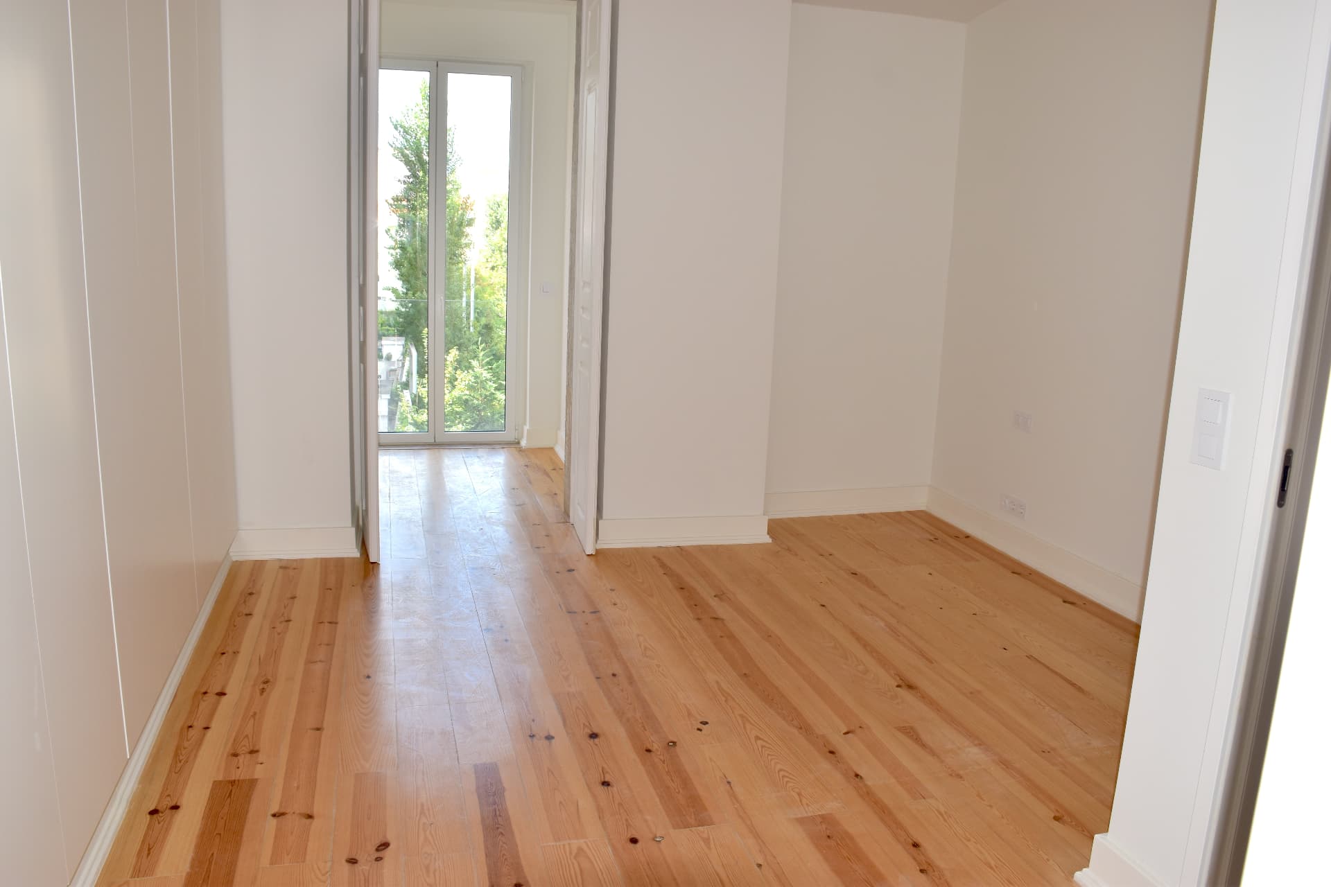 Quarto com porta de sacada e vista para a copa das árvores